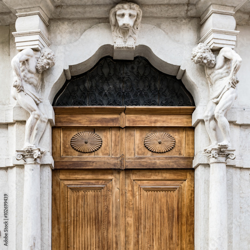 Old white stone entrance with statues and wooden portal.