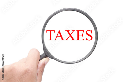 Hand showing Taxes word through magnifying glass. Magnifying glass search concept. Isolated on white background.