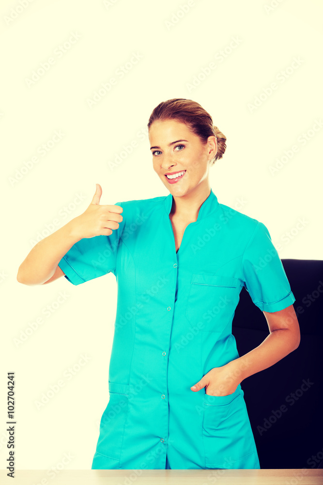 Female doctor standing behind the desk and swhows thumb up Female doctor standing behind the desk and swhows thumb up