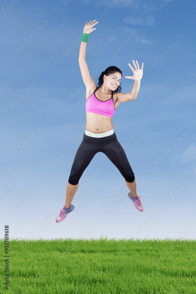 Excited woman jumping at field with sportswear Excited woman jumping at field with sportswear