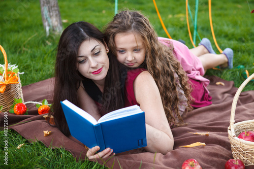 Mom and daughter reading a book lying on the plaid in the park