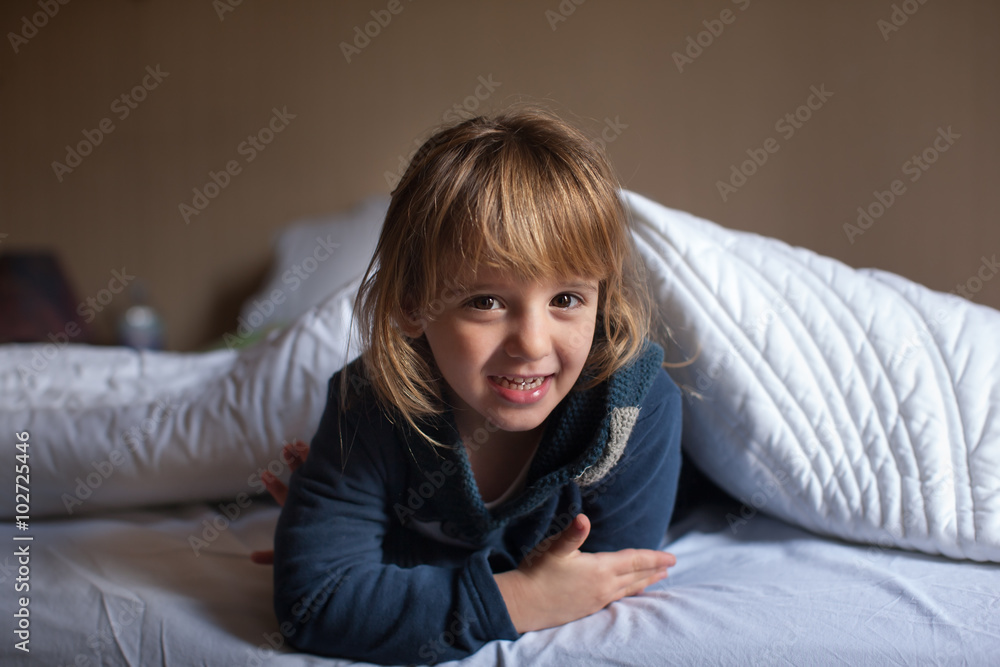 Obraz premium Bambina gioca a letto sotto il piumone