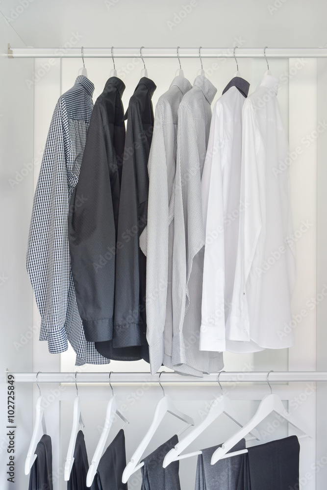 row of white, gray, black shirts with pants hanging in wooden wardrobe row of white, gray, black shirts with pants hanging in wooden wardrobe