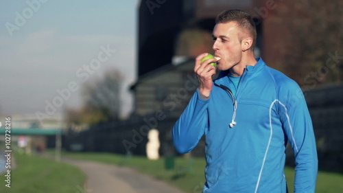 Young, handsome man eating apple in city while woman jogging  
