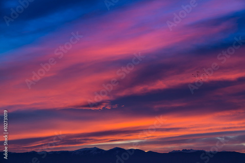 Fototapeta Naklejka Na Ścianę i Meble -  Sunset / sunrise with vivid magenta sky, clouds and mountains dark silhouettes.