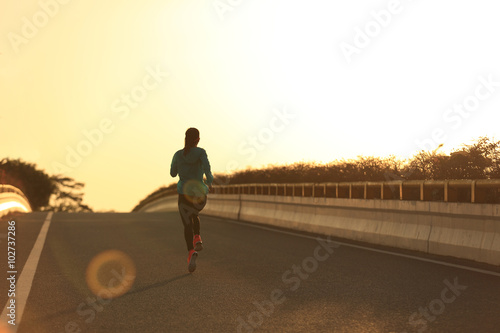 young fitness woman runner running on sunrise road