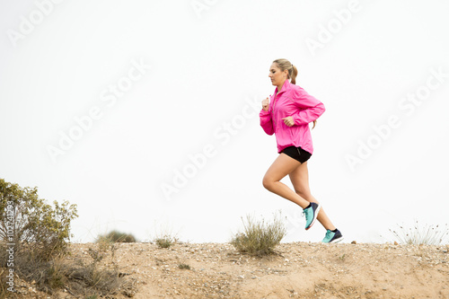 young sport woman running off road trail dirty road with dry desert landscape background training hard