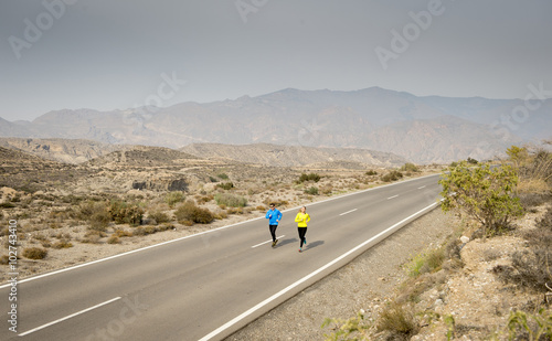 attractive sport couple man and woman running together on desert asphalt road mountain landscape