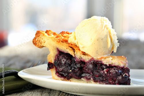 Slice of Blueberry Pie with vanilla ice cream on rustic wooden table