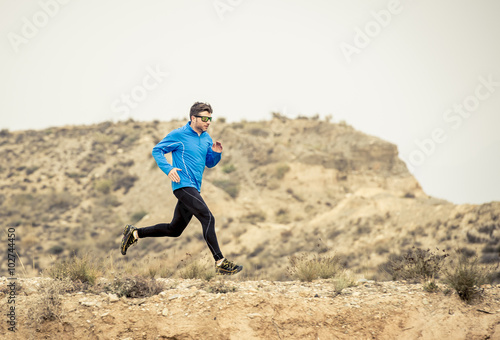 sport man running on off road trail dirty road with dry desert landscape background training hard