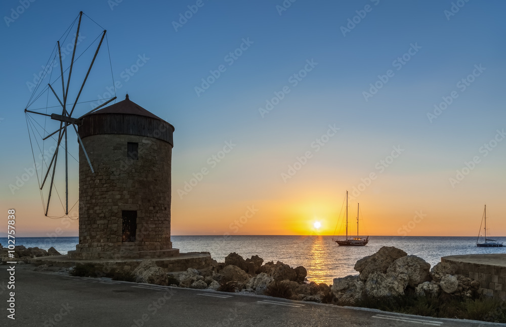 Mill on the background of the rising sun in the harbor of Mandraki. Rhodes Island. Greece