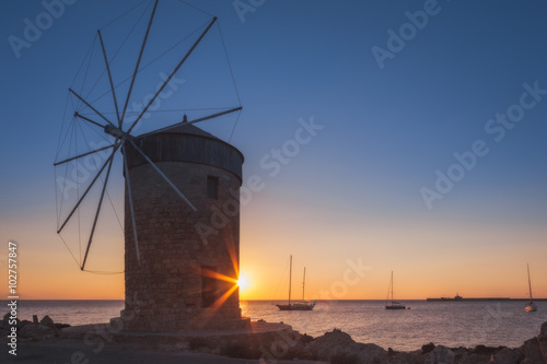 Mill on the background of the rising sun in the harbor of Mandraki. Rhodes Island. Greece