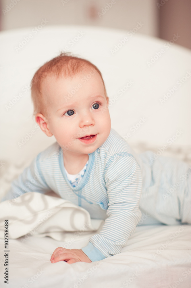 Smiling baby boy wake up in bed in room. Wearing pajamas. Looking away. Good morning. Smiling baby boy wake up in bed in room. Wearing pajamas. Looking away. Good morning.