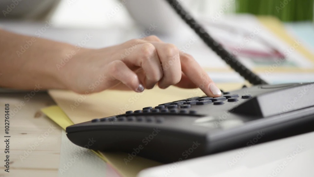 Woman at desk dialing a number and making a phone call using a telephone