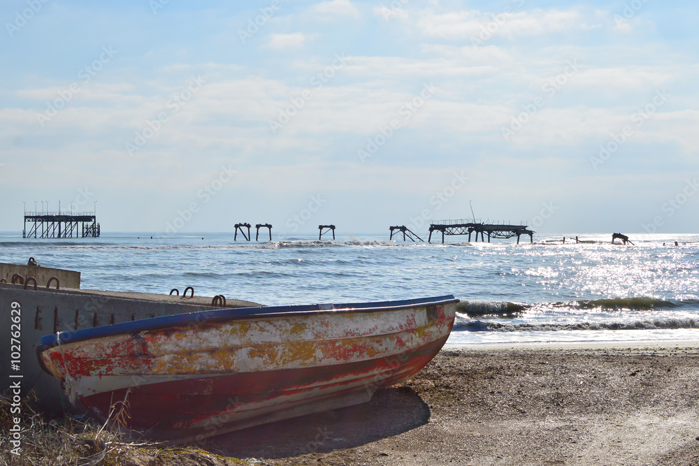 Old fishing boat on the beach, skeleton of ruined oil terminal seen on the horizon, Cape Shabla, Black Sea, Bulgaria
