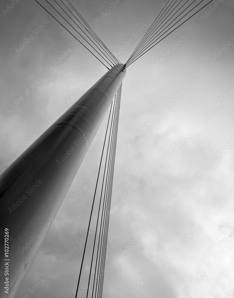 Fototapeta premium Pylon with cables, part of the structure of an urban bridge, against a dark, threatening sky.