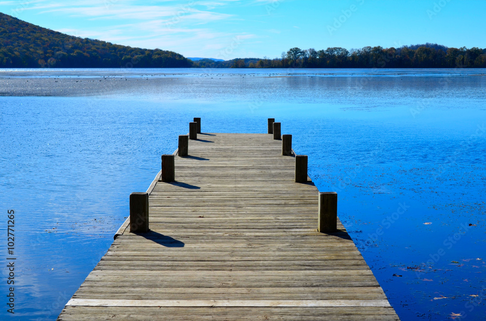 Naklejka premium Wooden dock pier extending over blue lake water.