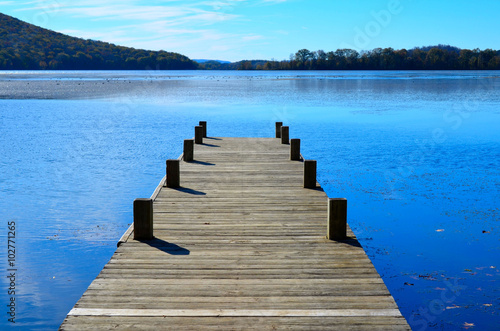 Fotótapéta Wooden dock pier extending over blue lake water.
