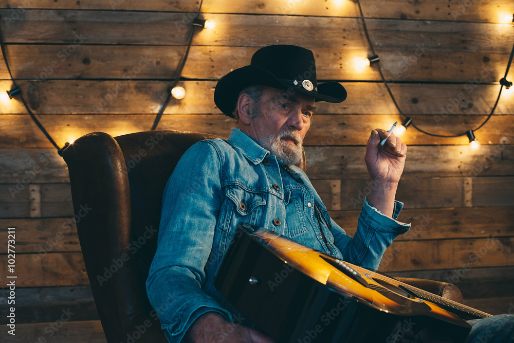 Fototapeta premium Smoking senior country and western guitarist with beard sitting