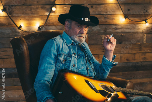 Smoking senior country and western guitarist with beard sitting