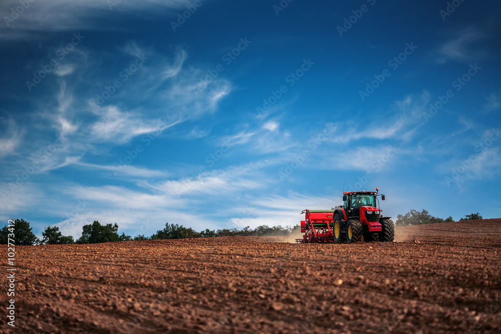 Naklejka premium Farmer with tractor seeding crops at field