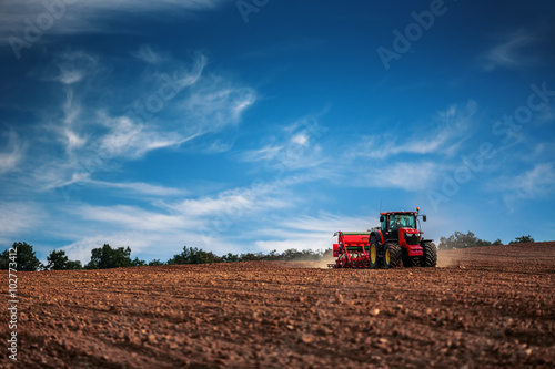 Fotografiet Farmer with tractor seeding crops at field