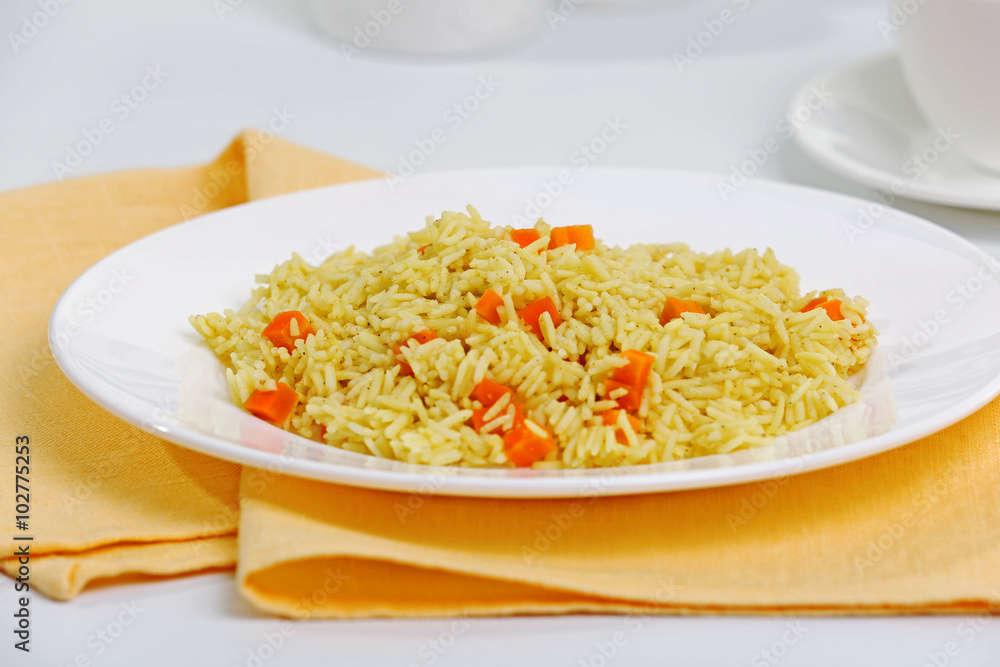 Stewed rice with a carrot on a white plate, close up