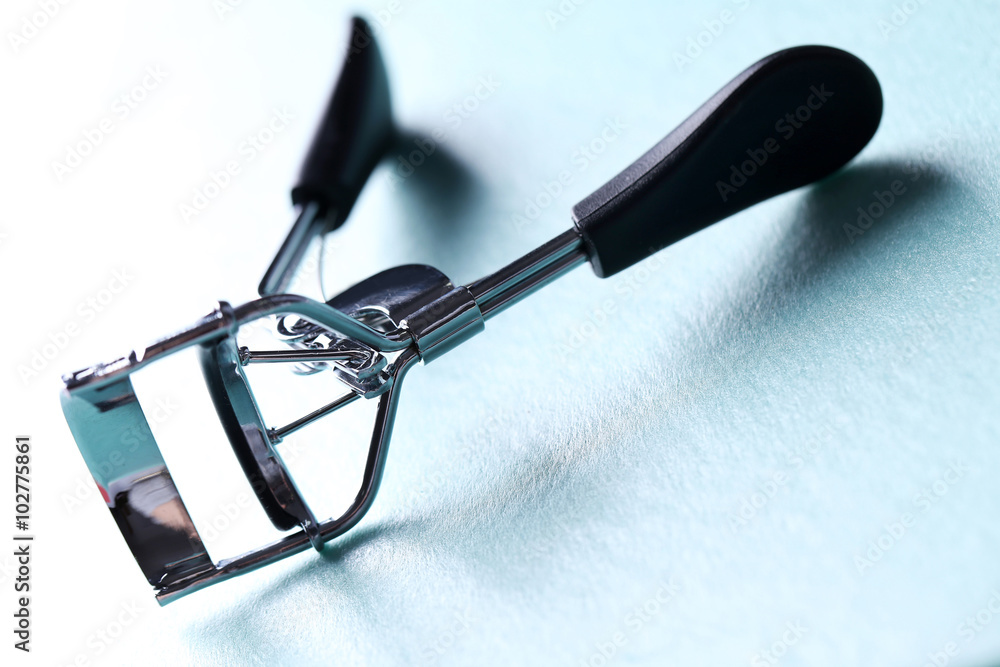 Eyelash curler with black handles on a blue background, close up