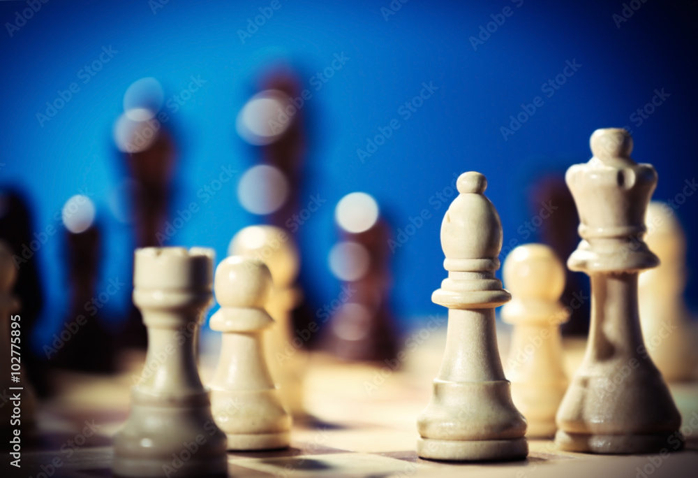 Chess pieces and game board on blue blurred background