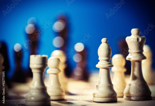 Chess pieces and game board on blue blurred background