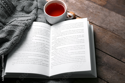 An open book, a cup of tea and a blanket on the wooden background