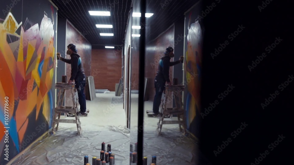 Graffiti artist painting on the wall with reflection in the column, interior Graffiti artist painting on the wall with reflection in the column, interior