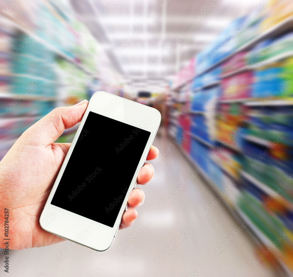 Female hand holding mobile smart phone on Supermarket blur background, business concept Female hand holding mobile smart phone on Supermarket blur background, business concept