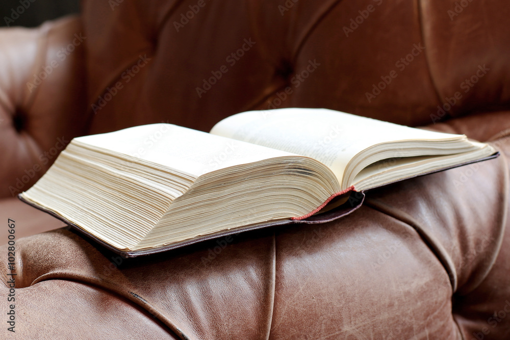 Thick book in hardcover on a leather sofa Thick book in hardcover on a leather sofa
