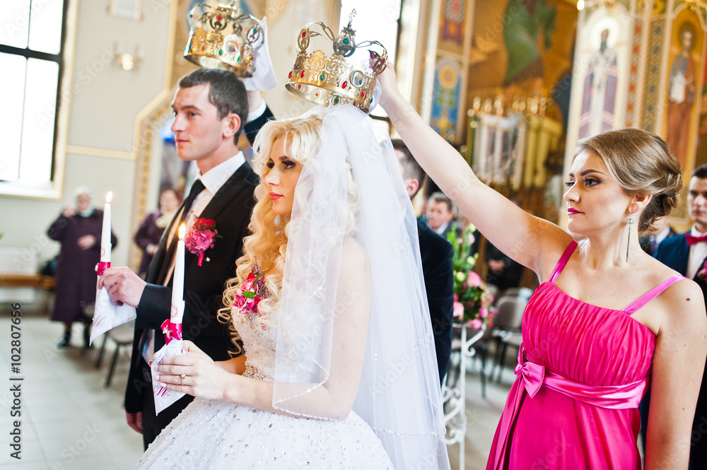 Bridesmaid holding crown on had of newlyweds at churh
