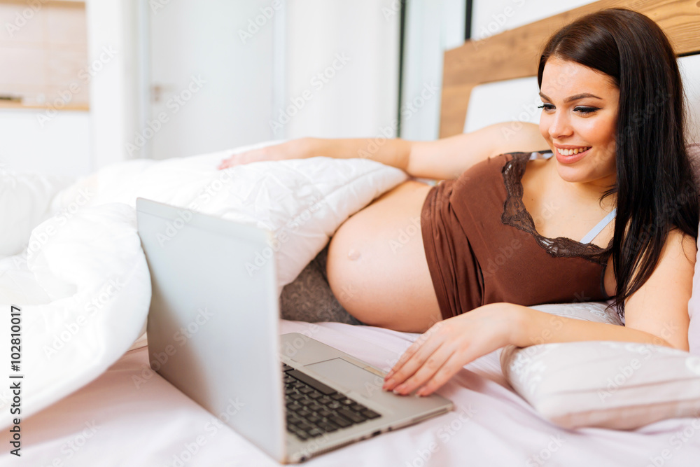 Pregnant woman using laptop in bed Pregnant woman using laptop in bed