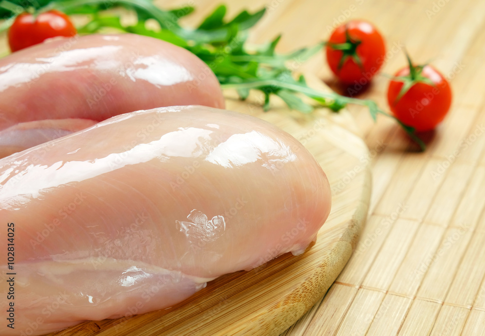 Raw chicken fillet with cherry tomatoes and arugula on a round bamboo cutting board. Raw chicken fillet with cherry tomatoes and arugula on a round bamboo cutting board.