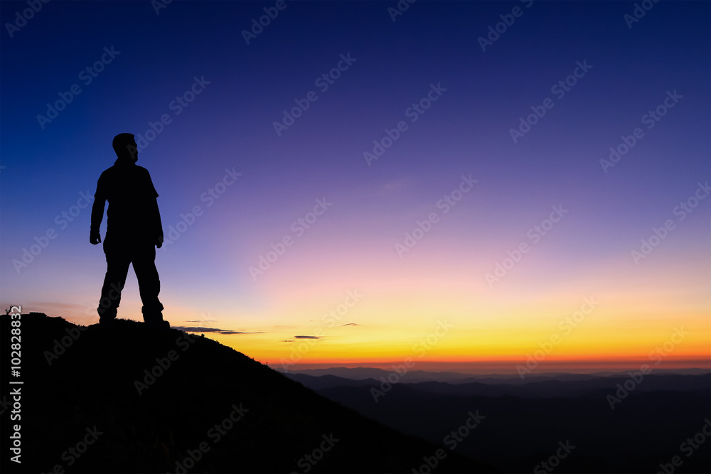 Silhouette of man standing on the top of mountain to enjoy colourful sky