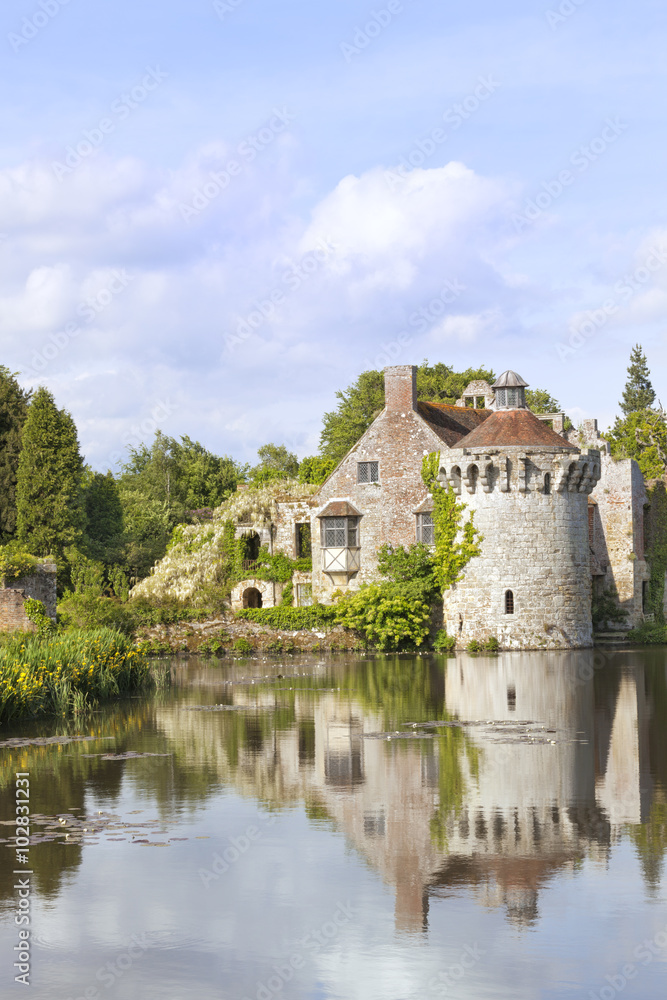 14th century moated English medieval castle Scotney in Kent countryside surrounded by romantic gardens, woodlands, with ruined castle reflected in the lake with floating water white lilies