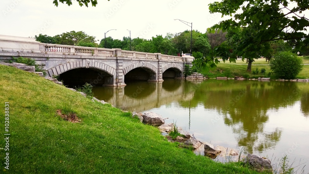 Old three arch bridge with green grass, trees and water in Delaware park, Buffalo New York