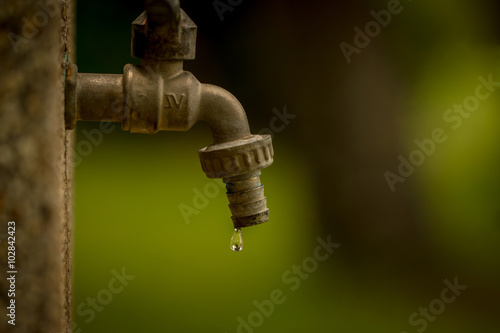 Water tap in park. Old and worn out, causing a water drop as consumption Resource. Consumption of water.