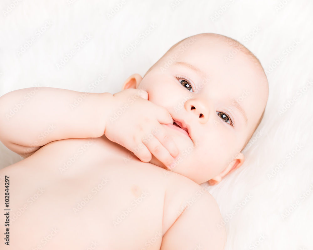 Closeup portrait of a cute smiling baby lying on white fur and sucking fingers Closeup portrait of a cute smiling baby lying on white fur and sucking fingers