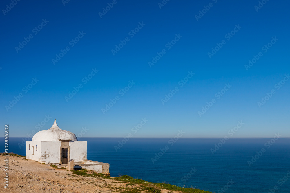 The remote Ermida da Memoria (Memory Hermitage) of the Nossa Senhora do Cabo Sanctuary, built on the edge of a cliff on Espichel Cape, with the Atlantic Ocean in background. Sesimbra, Portugal.