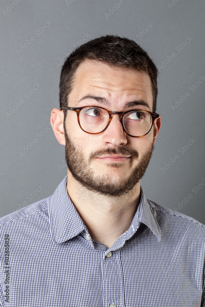 imagination concept - dubious 20s male manager with beard and eyeglasses thinking about an inspiring idea or inspiration, gray background. imagination concept - dubious 20s male manager with beard and eyeglasses thinking about an inspiring idea or inspiration, gray background.