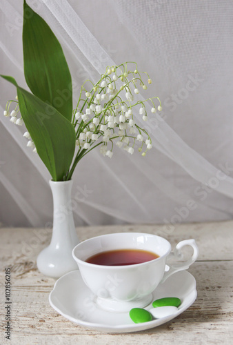 cup of tea and a bouquet of lilies of the valley in the vase