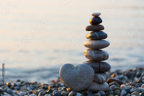 Grey stone in shape of heart in front of balanced stones on still water background photo