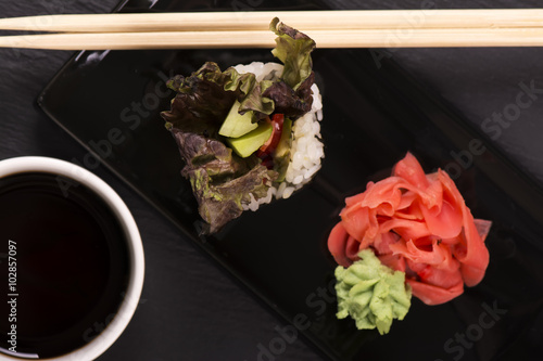 Vegetarian sushi roll served with wasabi, ginger and soy sauce over black stone background. Selective focus