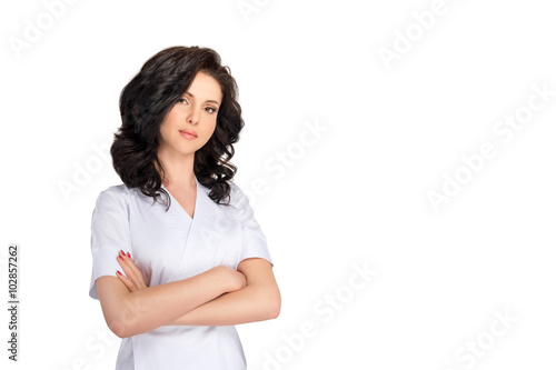 Young pretty female doctor in uniform keeping arms crossed and looking at camera isolated on white background. © Magryt