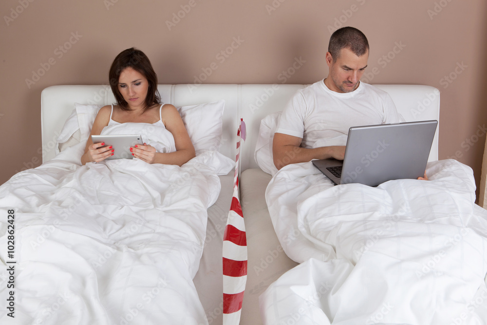 Young couple using tablet and computer in bed. Young couple using tablet and computer in bed.