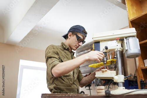 Young carpenter drilling wood element In goggles